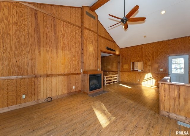 unfurnished living room featuring vaulted ceiling with beams, wood walls, light hardwood / wood-style floors, and ceiling fan