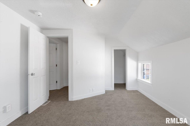 empty room featuring light colored carpet, a textured ceiling, and lofted ceiling