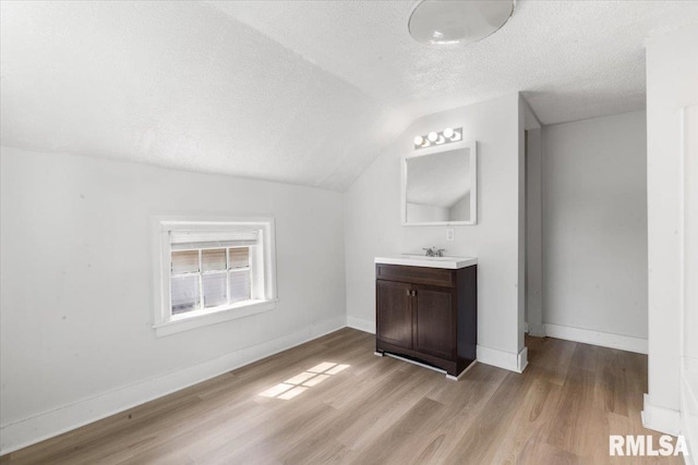 bathroom with wood-type flooring, vanity, lofted ceiling, and a textured ceiling