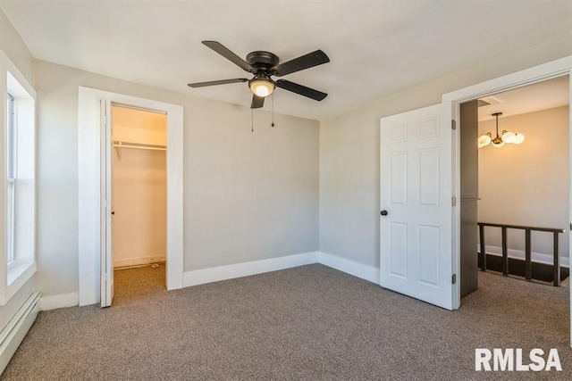 unfurnished bedroom featuring ceiling fan with notable chandelier, carpet flooring, a spacious closet, and a baseboard heating unit