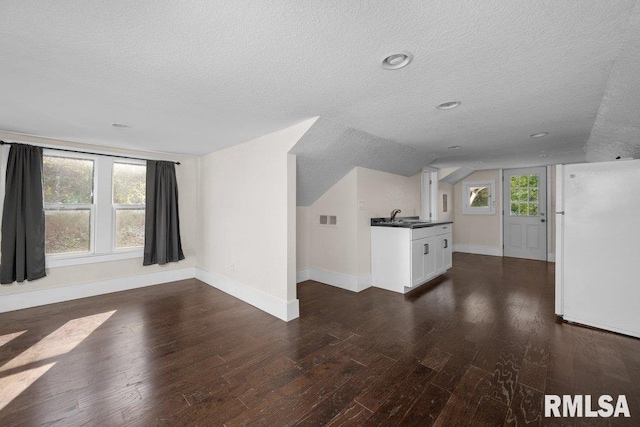 unfurnished living room with plenty of natural light, vaulted ceiling, dark hardwood / wood-style flooring, and a textured ceiling