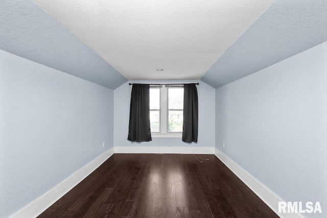 additional living space featuring dark wood-type flooring, vaulted ceiling, and a textured ceiling