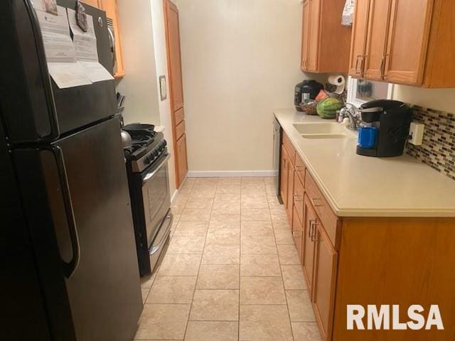 kitchen with appliances with stainless steel finishes, sink, light tile patterned floors, and tasteful backsplash