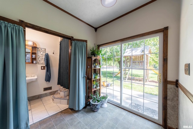 doorway featuring a textured ceiling, lofted ceiling, tile patterned flooring, and ornamental molding