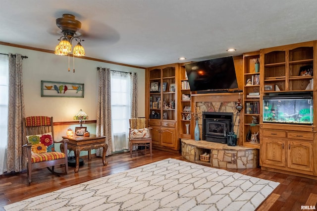 living room featuring ornamental molding, ceiling fan, a wood stove, and hardwood / wood-style flooring