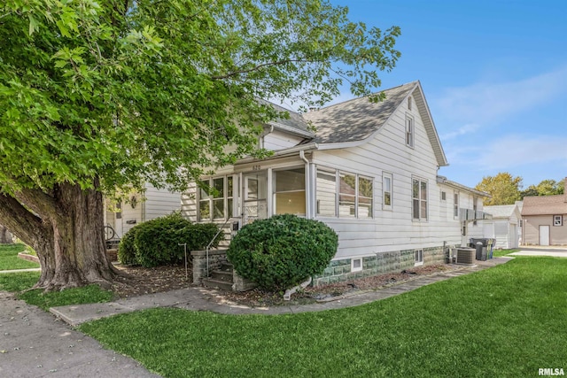 view of front of house with a front lawn, central air condition unit, a sunroom, and a shingled roof