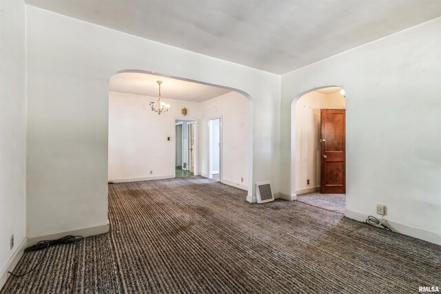 empty room with an inviting chandelier and dark colored carpet