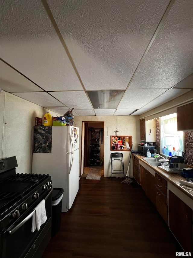 kitchen featuring white refrigerator, a drop ceiling, dark wood-type flooring, gas range, and sink