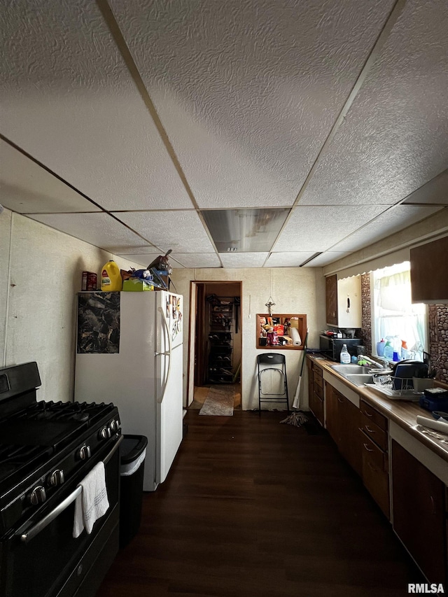 kitchen featuring freestanding refrigerator, a drop ceiling, dark wood-type flooring, a sink, and black range with gas cooktop