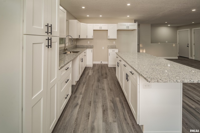 kitchen with light stone counters, a center island, white cabinets, sink, and dark hardwood / wood-style flooring