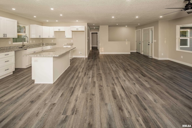 kitchen with a kitchen island, dark hardwood / wood-style flooring, light stone countertops, white cabinets, and a textured ceiling