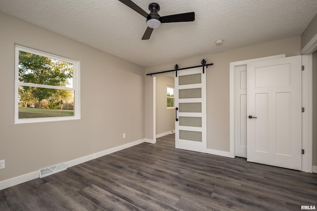 unfurnished bedroom featuring ceiling fan, a textured ceiling, a barn door, and dark hardwood / wood-style flooring