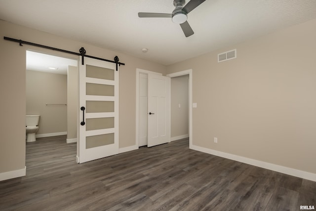 unfurnished bedroom with ceiling fan, dark wood-type flooring, ensuite bathroom, and a barn door