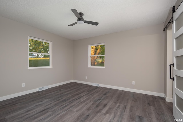 empty room with a barn door, dark hardwood / wood-style flooring, a textured ceiling, and a healthy amount of sunlight