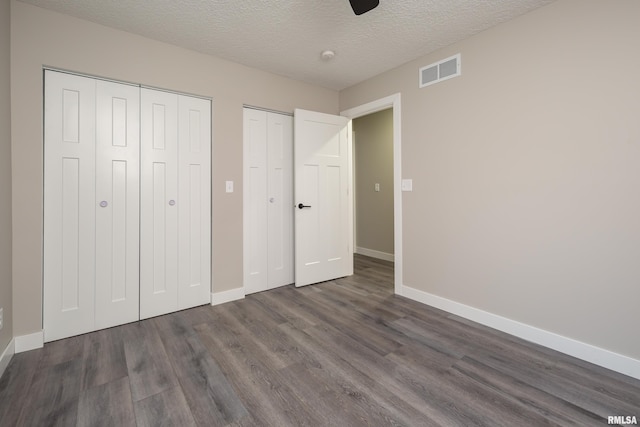 unfurnished bedroom with ceiling fan, dark hardwood / wood-style floors, multiple closets, and a textured ceiling