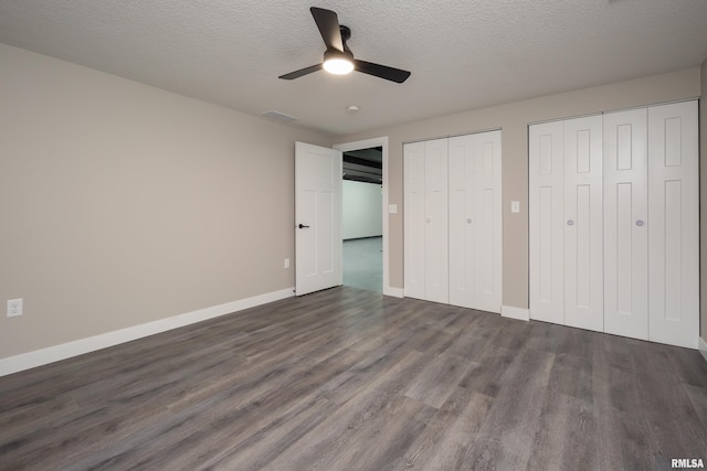 unfurnished bedroom featuring two closets, dark hardwood / wood-style flooring, a textured ceiling, and ceiling fan