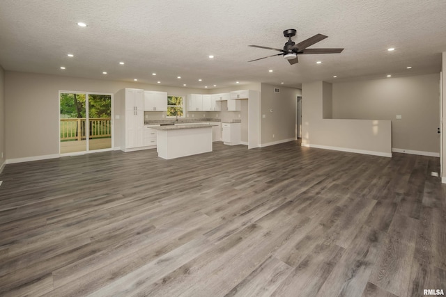 unfurnished living room with ceiling fan, a textured ceiling, and dark wood-type flooring