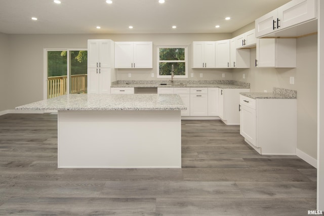 kitchen with a kitchen island, light stone countertops, white cabinets, sink, and dark hardwood / wood-style flooring