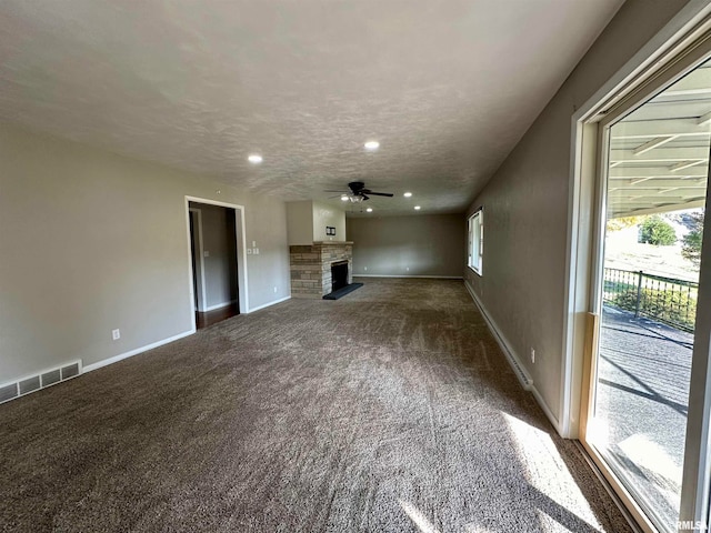 unfurnished living room with a fireplace, dark colored carpet, a textured ceiling, and ceiling fan