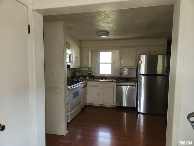 kitchen with sink, backsplash, white cabinetry, appliances with stainless steel finishes, and dark hardwood / wood-style flooring