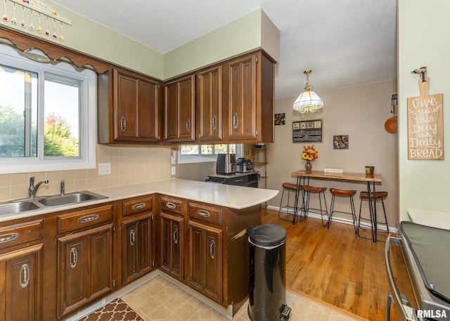 kitchen featuring light wood-type flooring, backsplash, sink, kitchen peninsula, and hanging light fixtures