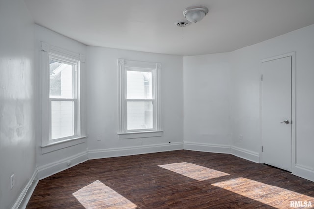 unfurnished room with baseboards, dark wood-type flooring, visible vents, and a healthy amount of sunlight