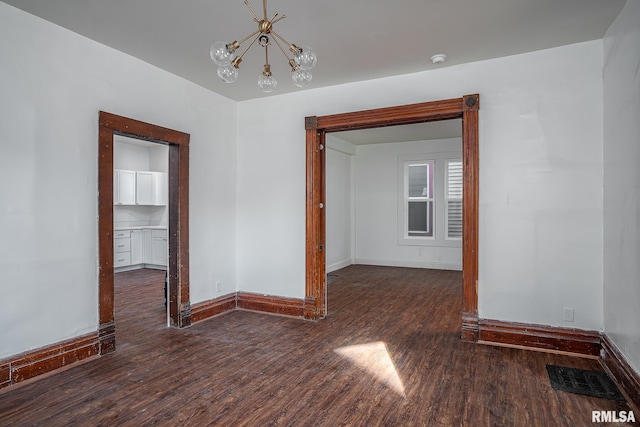 spare room with visible vents, dark wood finished floors, baseboards, and an inviting chandelier