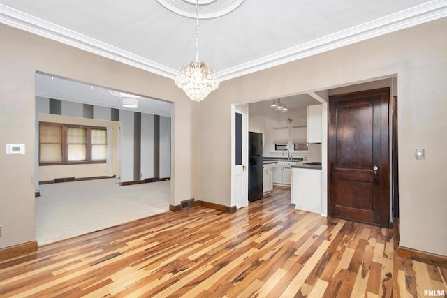 unfurnished dining area with ornamental molding, light wood-type flooring, and a notable chandelier