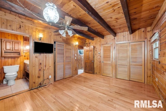 unfurnished bedroom with beamed ceiling, light hardwood / wood-style flooring, wooden walls, and two closets