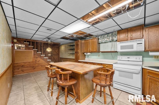 kitchen featuring a kitchen island, a kitchen breakfast bar, a drop ceiling, butcher block countertops, and white appliances