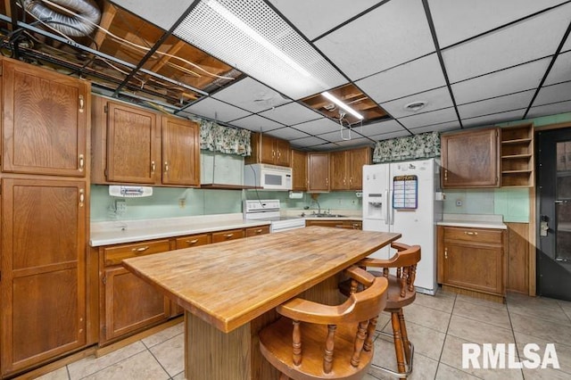 kitchen featuring a kitchen island, a kitchen breakfast bar, a paneled ceiling, light tile patterned flooring, and white appliances