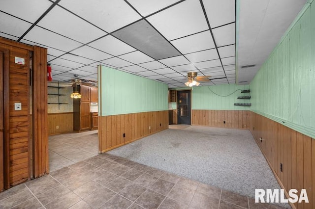 empty room with ceiling fan, wood walls, a paneled ceiling, and light colored carpet