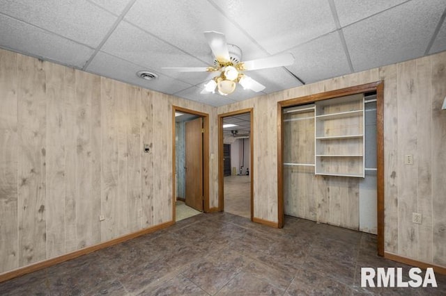 empty room with a paneled ceiling, wooden walls, and ceiling fan