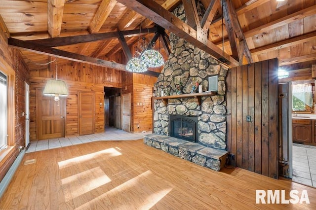 unfurnished living room featuring a stone fireplace, wood walls, beam ceiling, and light hardwood / wood-style floors