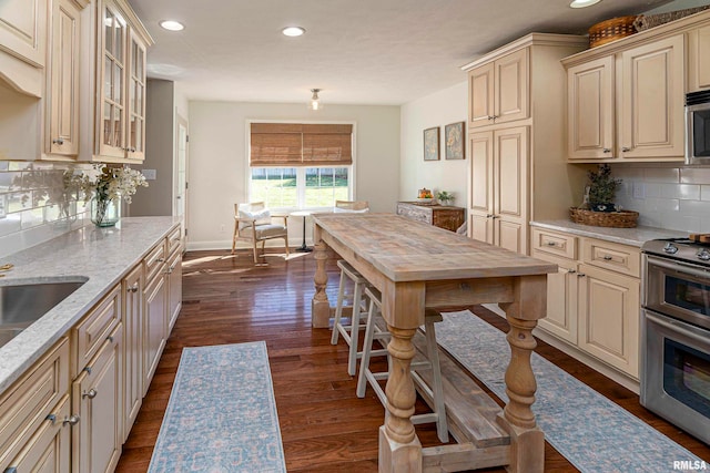 kitchen with tasteful backsplash, stainless steel appliances, light stone countertops, dark wood-type flooring, and cream cabinetry