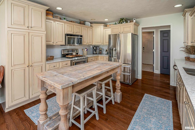 kitchen featuring stainless steel appliances, light stone counters, backsplash, cream cabinetry, and dark hardwood / wood-style flooring