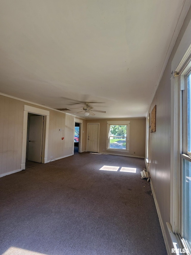 carpeted spare room with wood walls, crown molding, and ceiling fan