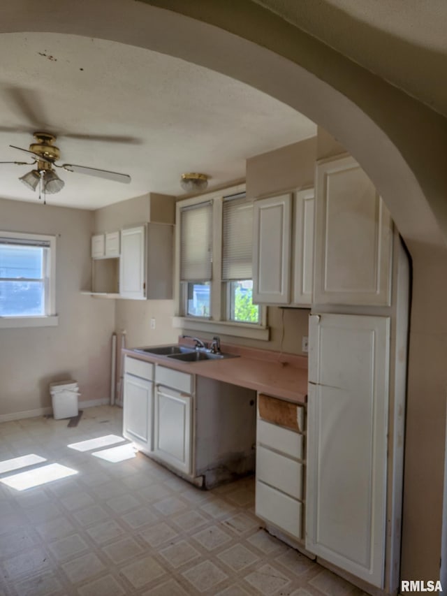 kitchen featuring ceiling fan, white cabinets, built in desk, and sink