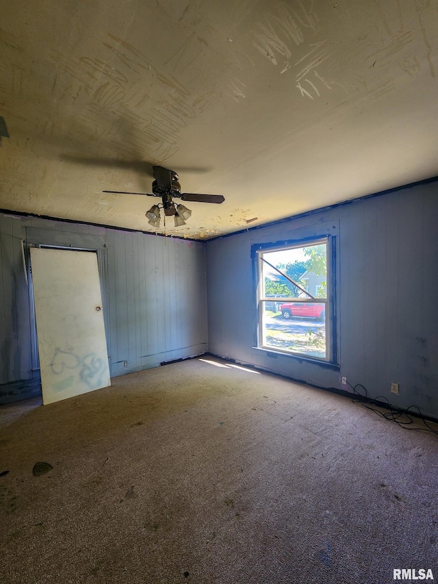 carpeted spare room featuring ceiling fan and wood walls