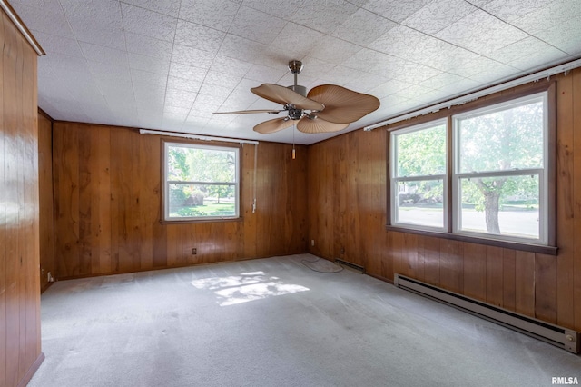 empty room featuring a baseboard radiator, wooden walls, and a healthy amount of sunlight