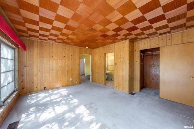 unfurnished bedroom with a closet, wooden ceiling, ensuite bathroom, and wooden walls