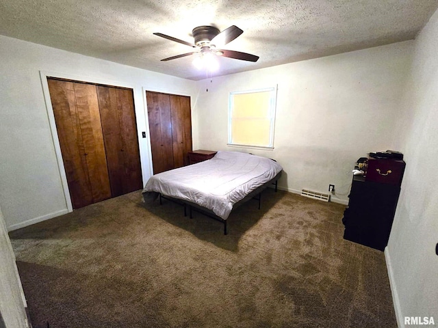 bedroom with ceiling fan, multiple closets, a textured ceiling, and dark colored carpet