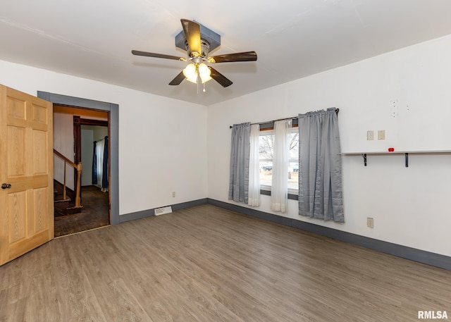 empty room featuring visible vents, baseboards, a ceiling fan, stairway, and wood finished floors