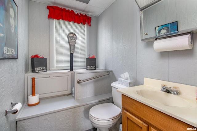 bathroom with toilet, vanity, and wooden walls