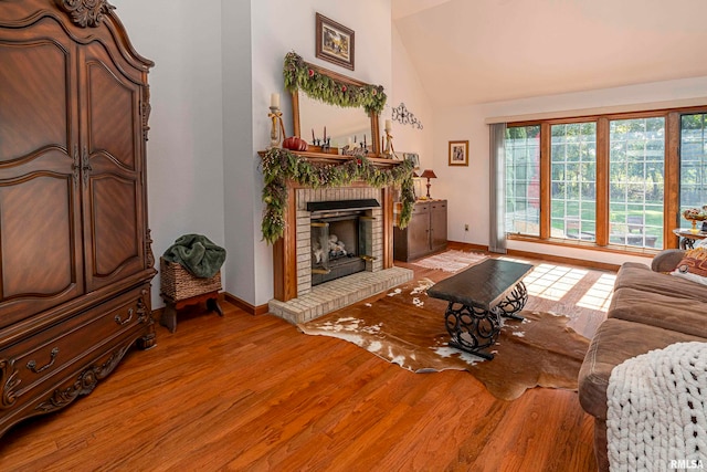 living room with a brick fireplace, hardwood / wood-style floors, and vaulted ceiling