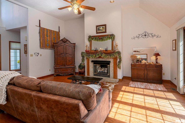 living room with light hardwood / wood-style floors, high vaulted ceiling, a fireplace, and ceiling fan