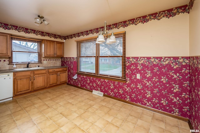 kitchen with sink, white dishwasher, pendant lighting, and a notable chandelier