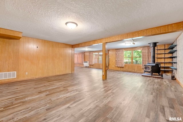 basement with light hardwood / wood-style floors, wood walls, a wood stove, and a textured ceiling