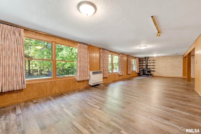 unfurnished living room with wooden walls, a textured ceiling, light wood-type flooring, and a wood stove