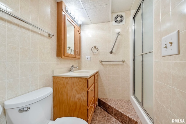 bathroom with toilet, a shower with shower door, vanity, and tile walls